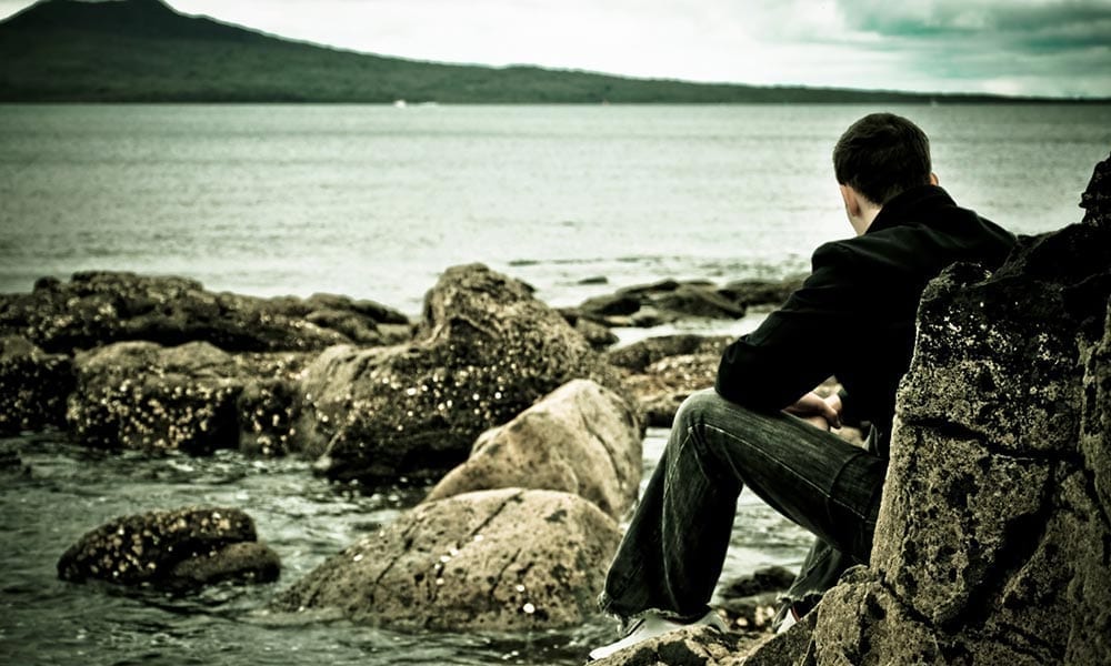 Photo of adolescent sitting near the water, thinking.